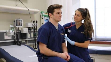 A female nursing student performs a hands-on assessment on a male classmate in the nursing simulation lab at Widener University