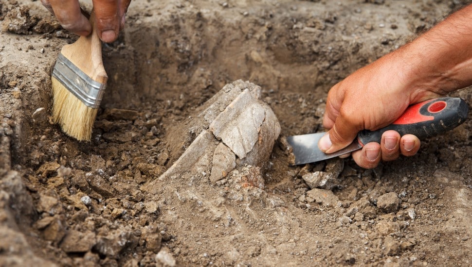 Archaeological excavations, archaeologists work, dig up an ancient clay artifact with special tools in soil
