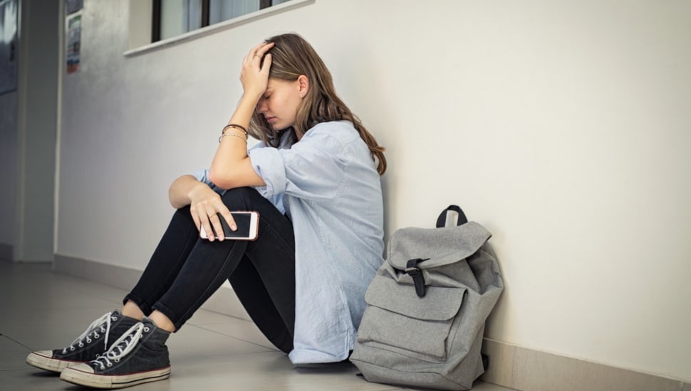 An anxious girl sitting in a hallway next to her book bag
