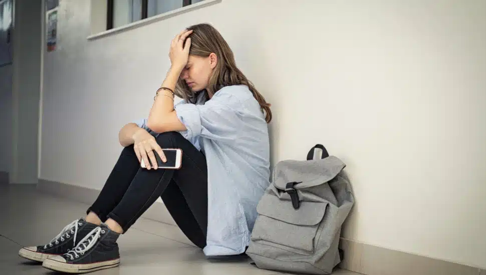 An anxious girl sitting in a hallway next to her book bag