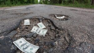 Dollar bills in the potholes on road illustrate the cost of pothole vehicle repairs