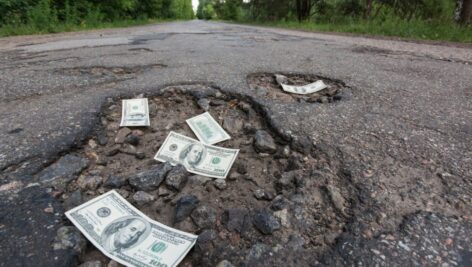 Dollar bills in the potholes on road illustrate the cost of pothole vehicle repairs