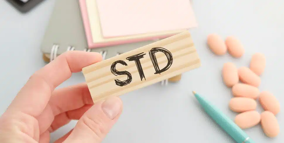 A hand is holding a wooden cube with an STD text next to some pills.