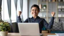 Woman at her laptop holds her arms in triumph after getting a job offer