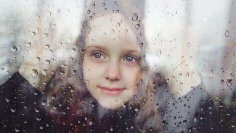 A sad little girl looking out of a window on a rainy day