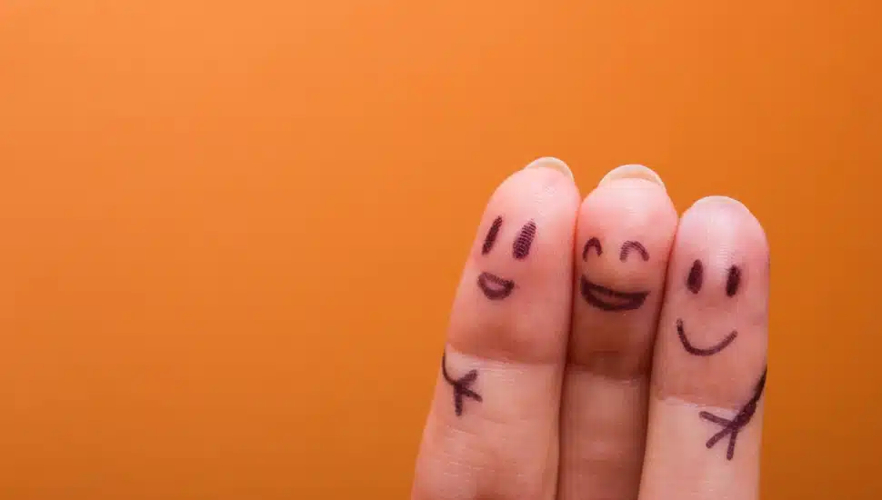 Three fingers side by side with happy faces and hugging arms drawn on them