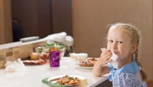 Little girl wiping her mouth with a napkin sitting at the table before a plate of pizza
