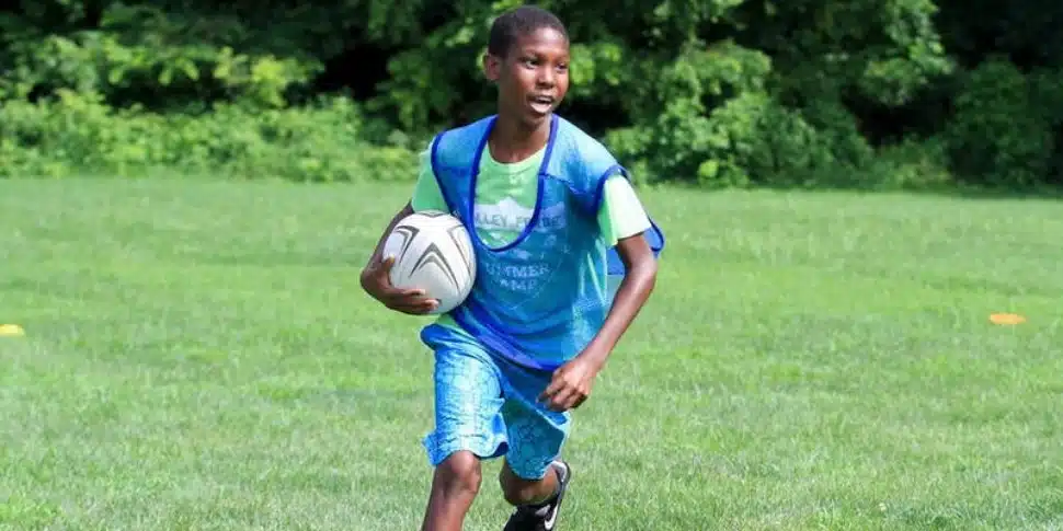 A little boy holding a soccer ball out in a grassy field at the Valley Forge Summer Camp.