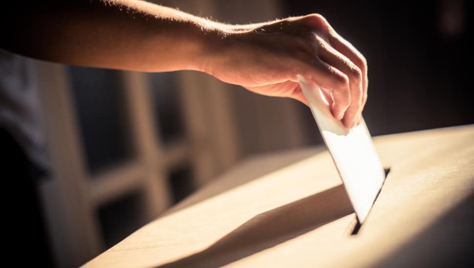 A hand placing a ballot in a wooden ballot box.