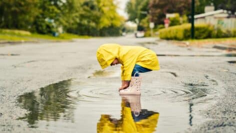 Little boy in a raincoat playing in a puddle