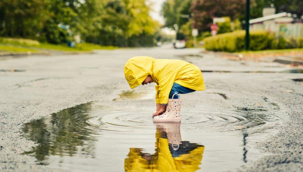 Little boy in a raincoat playing in a puddle