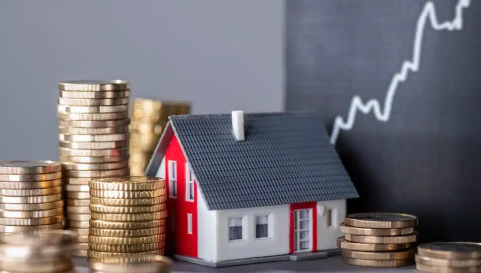 A house with stacks of money and a rising curve symbolizing a rise in home value.