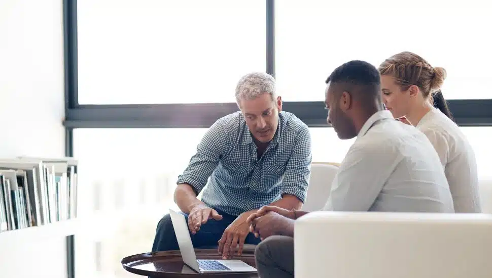 A man helping a man and woman while looking at a omputer