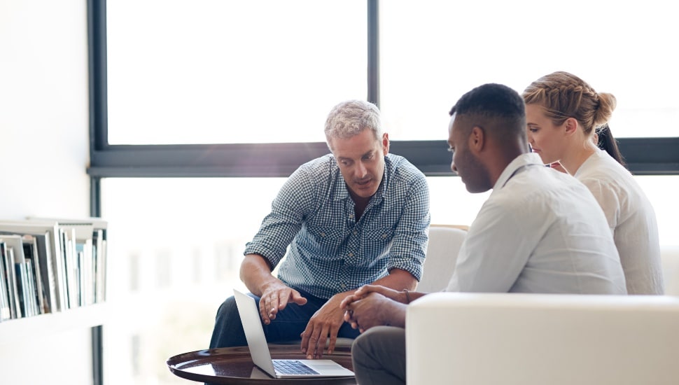 A man helping a man and woman while looking at a omputer