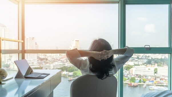 business woman relaxing in office hands behind head looking out window, work life balance