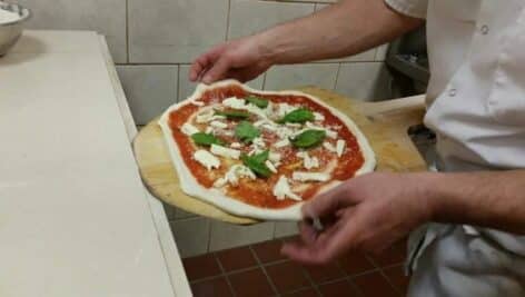 A Neapoliotan pizza with toppings is ready to go into a wood-fired oven for baking.