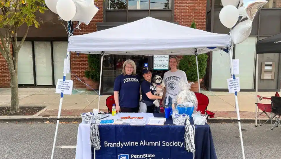 Three women with the Brandywine Alumni Society stand under a white tent at Media Borough's Dining Under the Stars.
