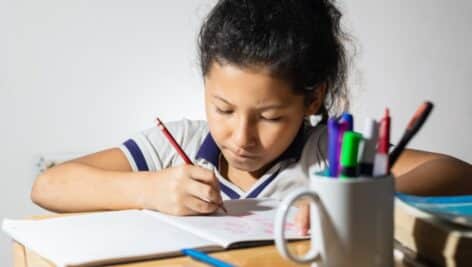 A little girl doing her homework at a school desk.
