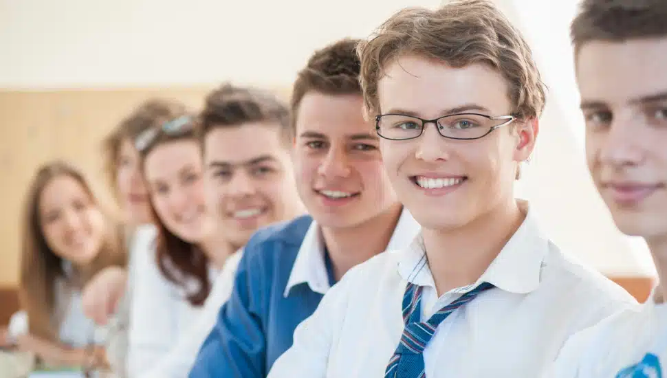 A group of happy teenage students standing in a row in a classroom.