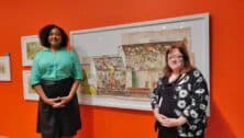 Co-curators Shadra Strickland and Audrey Lewis stand in front a large paper dollhouse Sophie Blackall created to illustrate her 2022 book, “Farmhouse.”