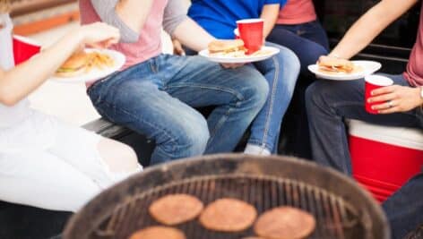 A group of friends eating hamburgers around a grill.