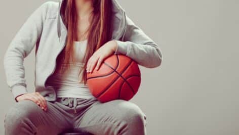 A woman basketball player seated, holding a basketball.