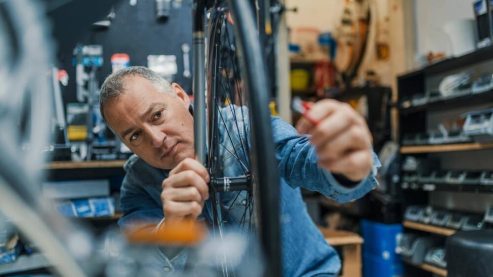A veteran business owner works on a bicycle wheel in his shop.