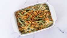 A traditional green bean casserole topped with French Fried Onions and cream of mushroom on white marble.
