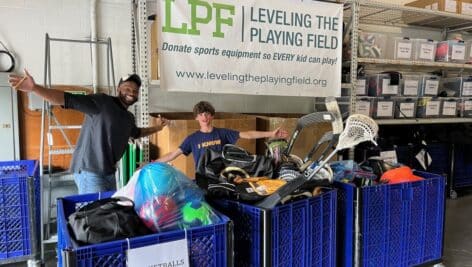 Two boys look happy standing behind containers of sports equipment at Leveling the Playing Field.