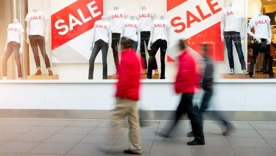 Shoppers rush past shop windows covered with "Sale" signs.