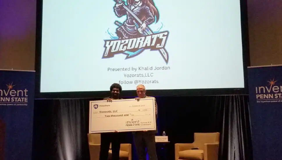 Khalid Jordan holds a large check for $2,000 with an Invent Penn State representative.