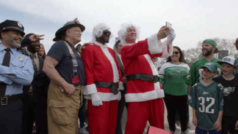Peyton Manning dressed as Santa poses with other people.