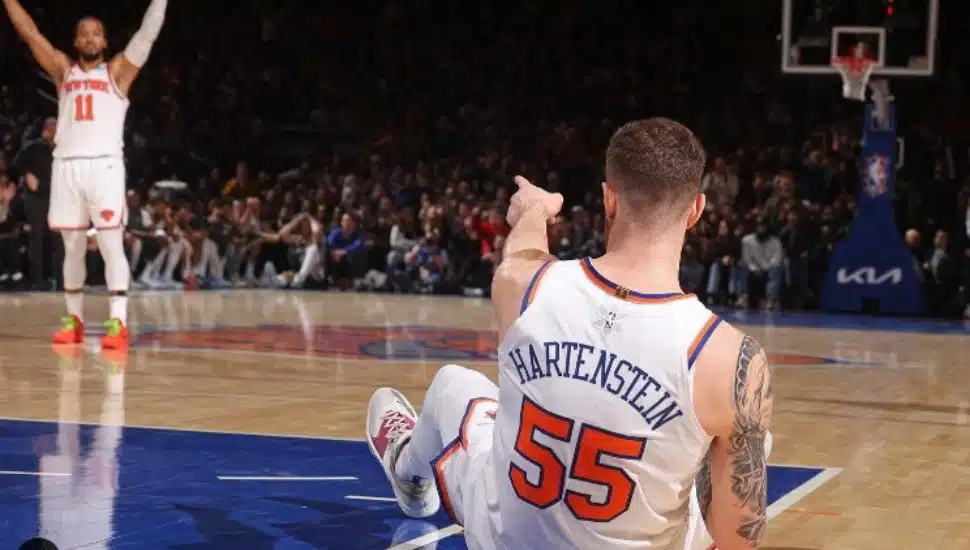 Jalen Brunson holds his arms up in victory on the basketball court as fellow Knicks player Isaiah PJ Hartenstein looks on.