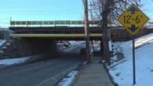 The road running under the Prospect Park Amtrak bridge with a sign indicating the bridge clearance height.