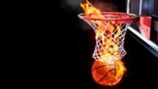 A basketball on fire going through the hoop on a basketball court.