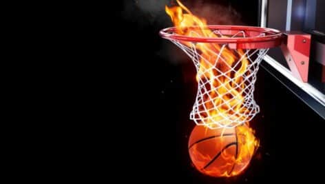 A basketball on fire going through the hoop on a basketball court.