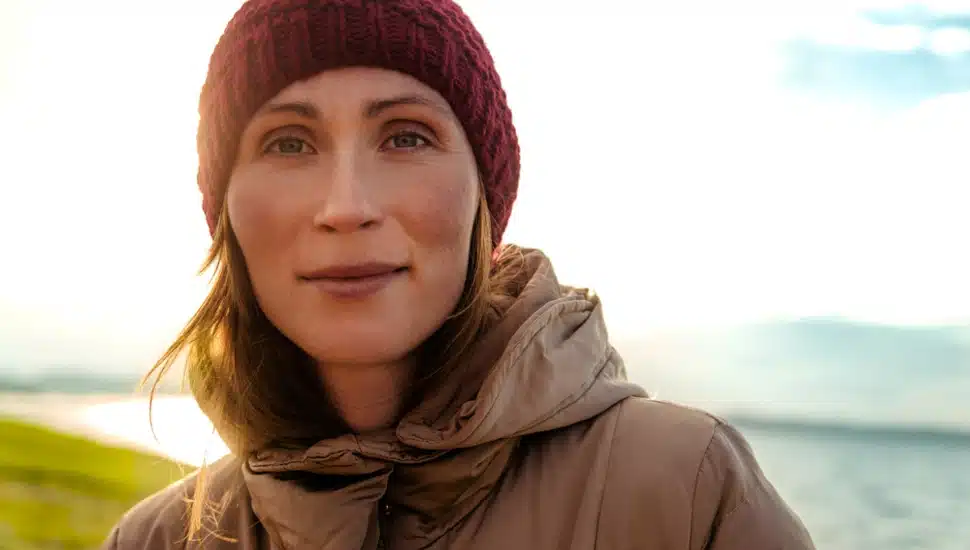A woman on a cold, sunny day standing outside by a lake.