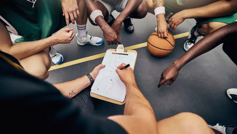 Basketball players huddle together with a coach as he goes over a roster.