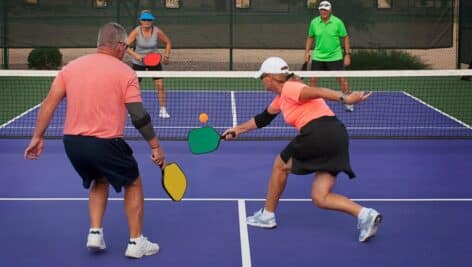 Four senior citizens play a round of Pickleball on a Pickleball court.