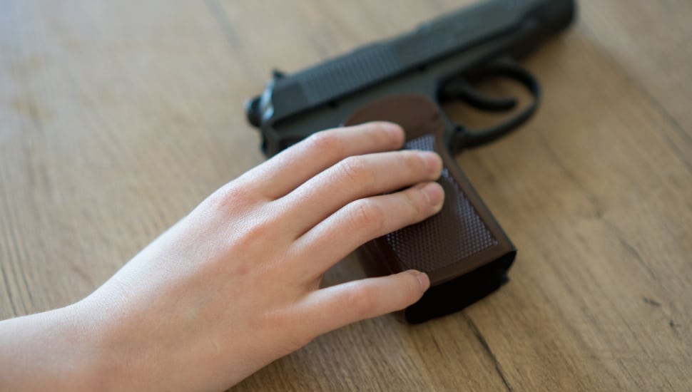 A child reaches for a pistol on a table.
