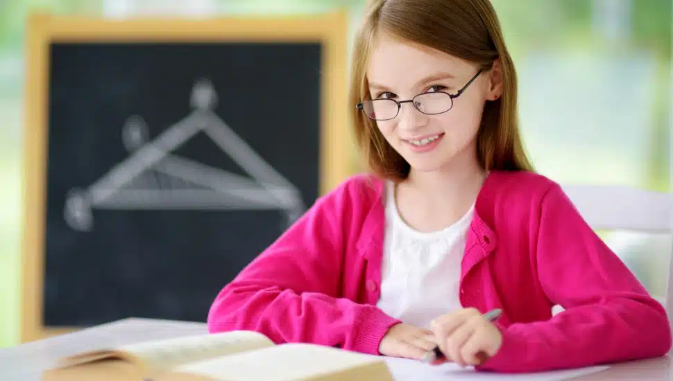 A studious middle school student sits at her desk with a text book open.