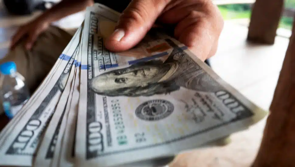 A hand is holding several $100 bills.