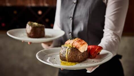 A surf and turf meal offered up by a uniformed waiter.