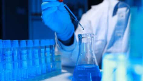 A researcher in a lab coat tests a chemical surrounded by lab equipment.