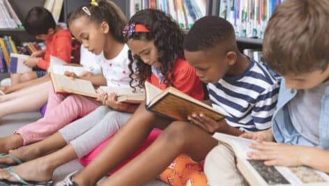 A group of children sitting on the floor of the library reading books.