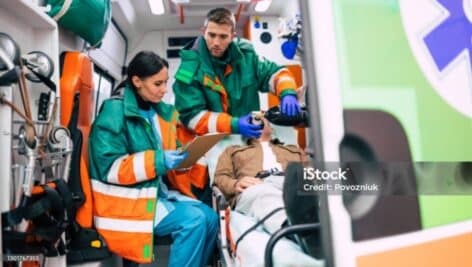 Paramedics inside an ambulance help a man in his 20s lying on a stretcher.