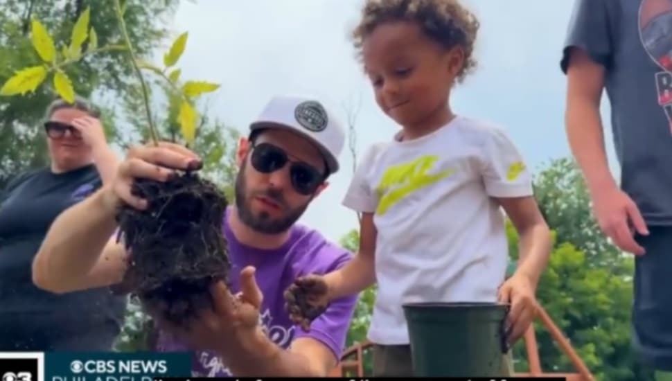 Erik Schroeder, a board member with Grands Stepping Up, gets ready to add a plant to the community garden as a young child looks on.