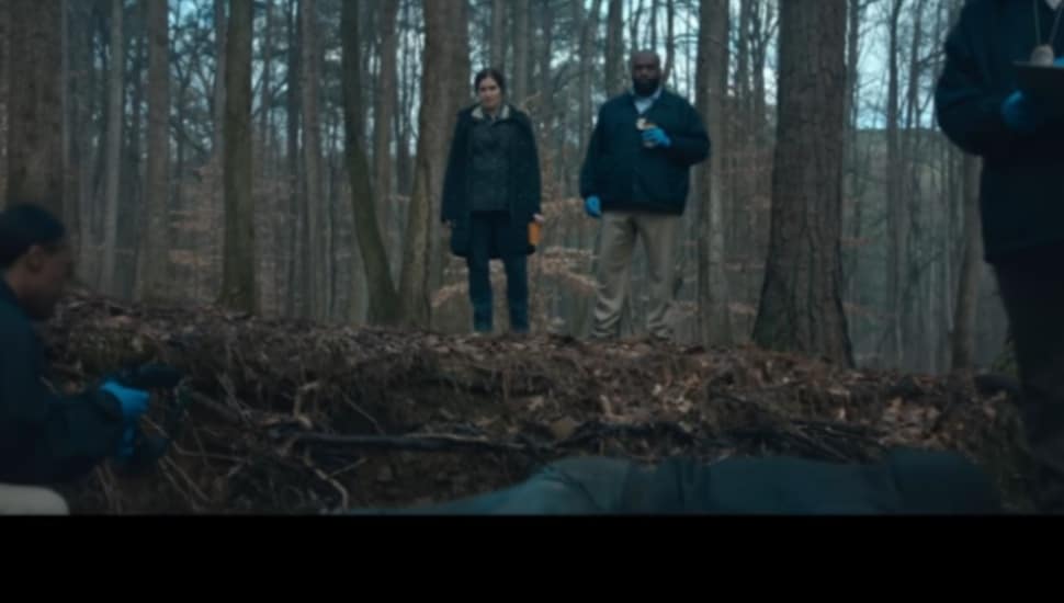 A "Mare of Easttown' shot of a woman detective and a coworker looking down on a body in the woods.