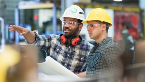 Construction management workers in hardhats, with one guiding a student.