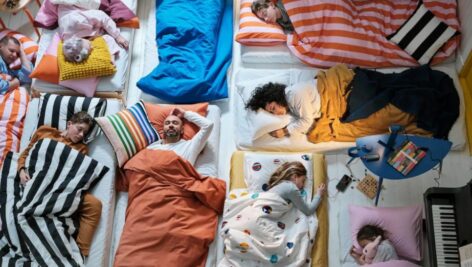 Several people in a shared room are asleep on beds.